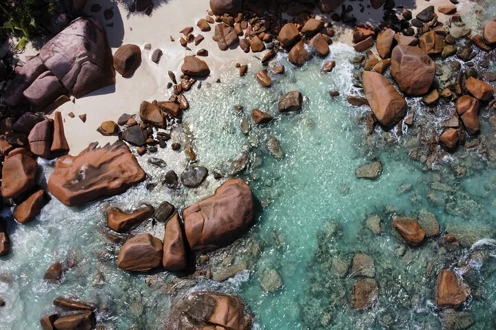 Top-down aerial view of clear shallow water between beach boulders